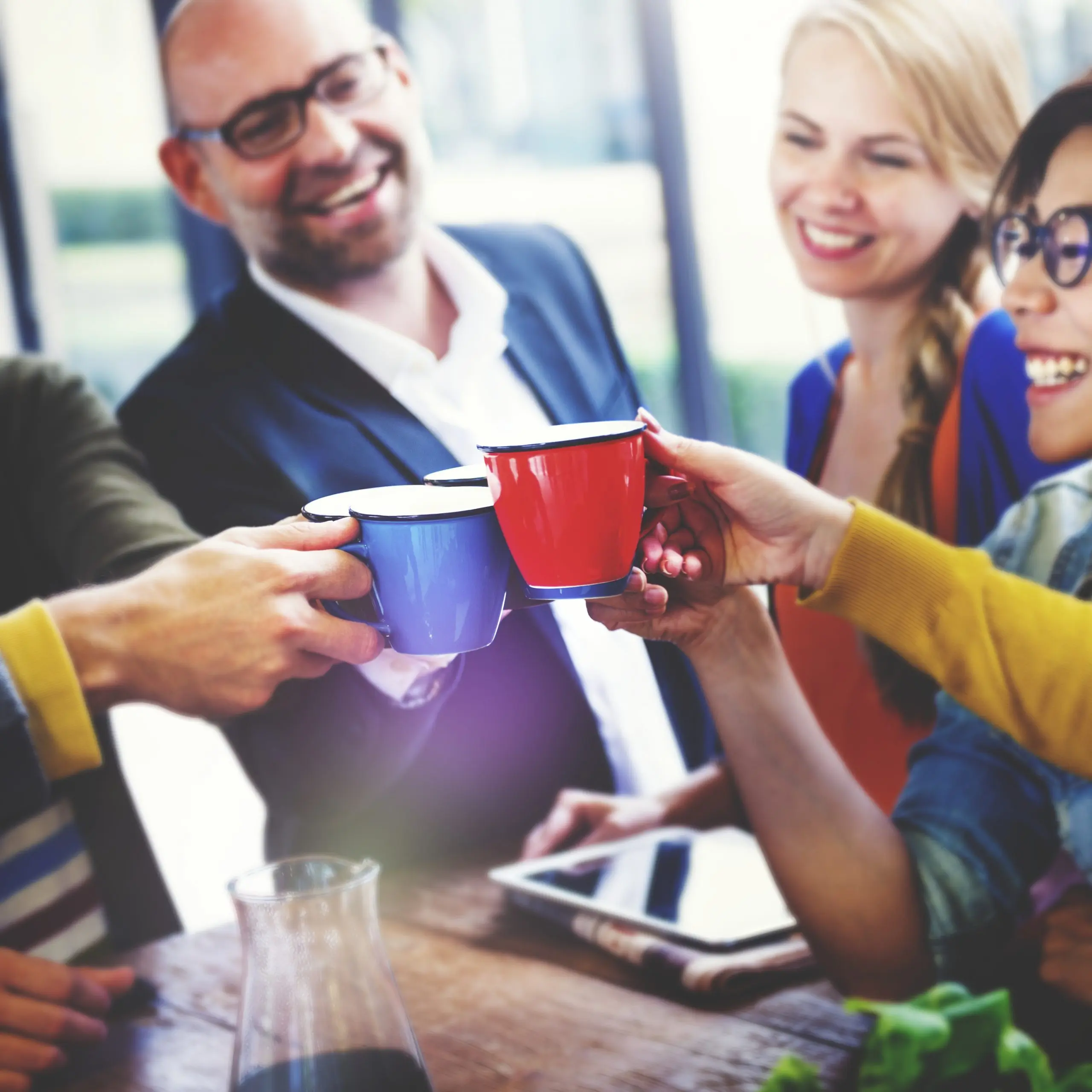 Multiethnische Gruppe feiert Ggeschäftserfolg Eine multiethnische Gruppe von fünf Personen, die mit bunten Tassen anstoßen, symbolisiert die Förderung einer inklusiven Unternehmenskultur zur Produktivitätssteigerung und Fluktuationsverringerung.