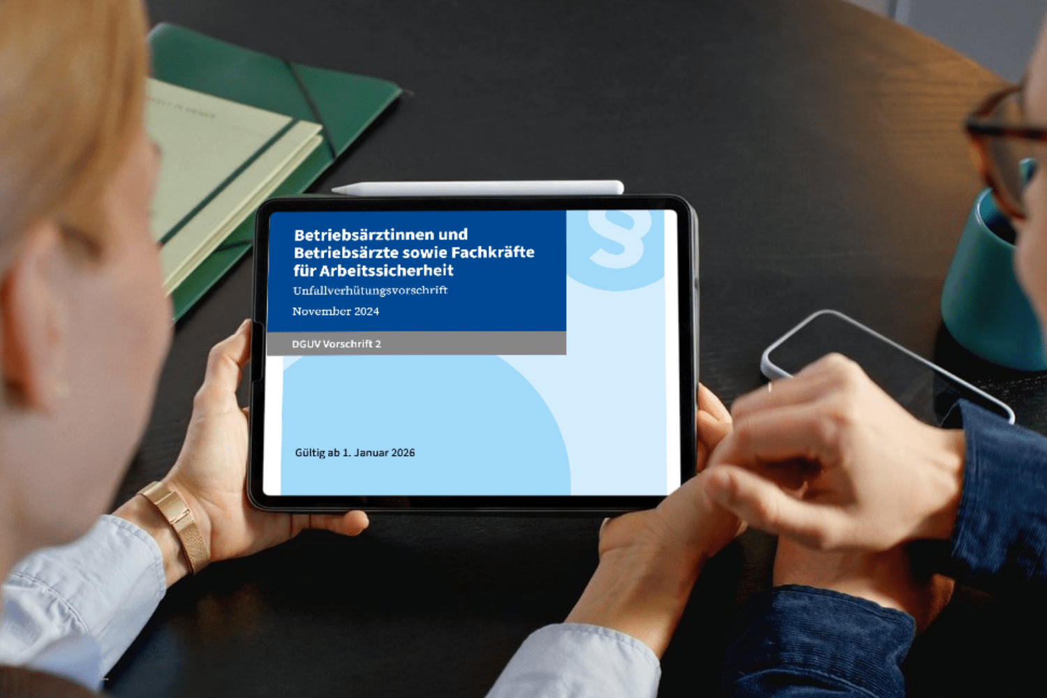 Zwei Personen betrachten ein Tablet, auf dem die DGUV Vorschrift 2 zur Arbeitssicherheit mit Gültigkeit ab 1. Januar 2026 angezeigt wird.